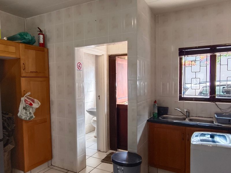 A functional kitchen featuring wooden cabinetry, tiled walls, and a double sink, with an adjacent utility area visible through the doorway.