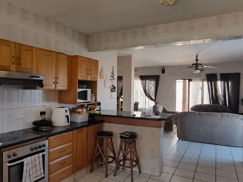 Open-plan kitchen and living area featuring wooden cabinetry, granite countertops, and tiled flooring, creating a functional and connected living space.