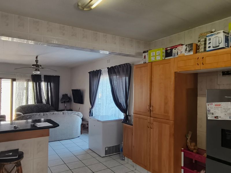 Open-plan living and kitchen area featuring tiled flooring, built-in wooden cabinetry, a breakfast counter, and sliding door access to the exterior.