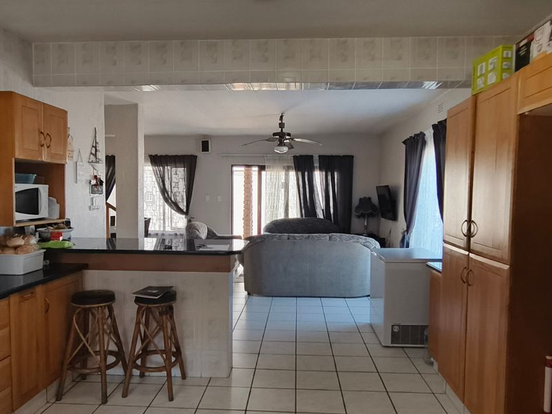 Open-plan kitchen and living area featuring wooden cabinetry, granite countertops, a breakfast bar, and tiled flooring throughout.