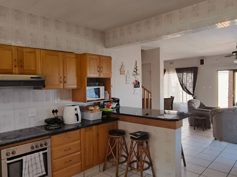 Open-plan kitchen and living area featuring wooden cabinetry, granite countertops, built-in appliances, and a breakfast bar, flowing into a spacious lounge.