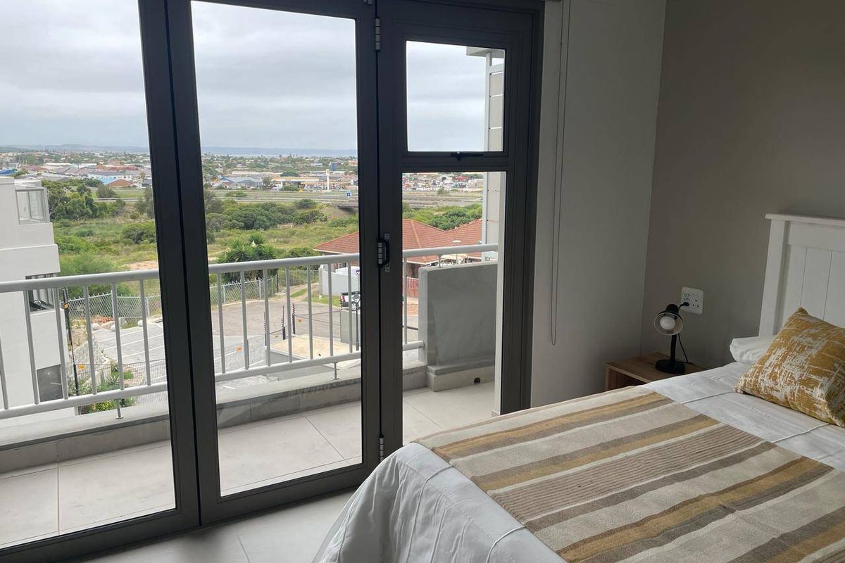 A bright bedroom featuring large aluminium sliding doors that open onto a private balcony with expansive neighbourhood views.