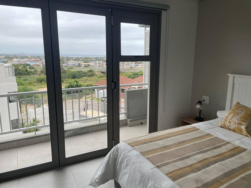 A bright bedroom featuring large aluminium sliding doors that open onto a private balcony with expansive neighbourhood views.