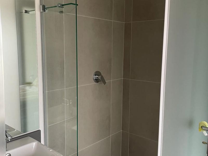 Modern bathroom featuring a walk-in shower with a rain shower head, glass screen, and a contemporary vanity basin with storage.