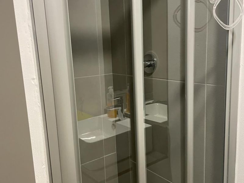 A compact bathroom shower enclosure featuring modern grey wall tiles and a glass door.