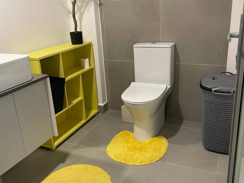 A modern bathroom featuring large format grey tiling, a wall-mounted vanity with a vessel sink, and a standard toilet.