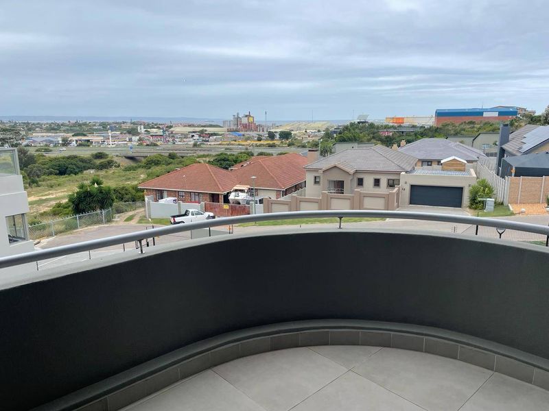 A curved balcony with a modern metal balustrade and tiled flooring, offering an elevated view over the surrounding residential neighborhood.