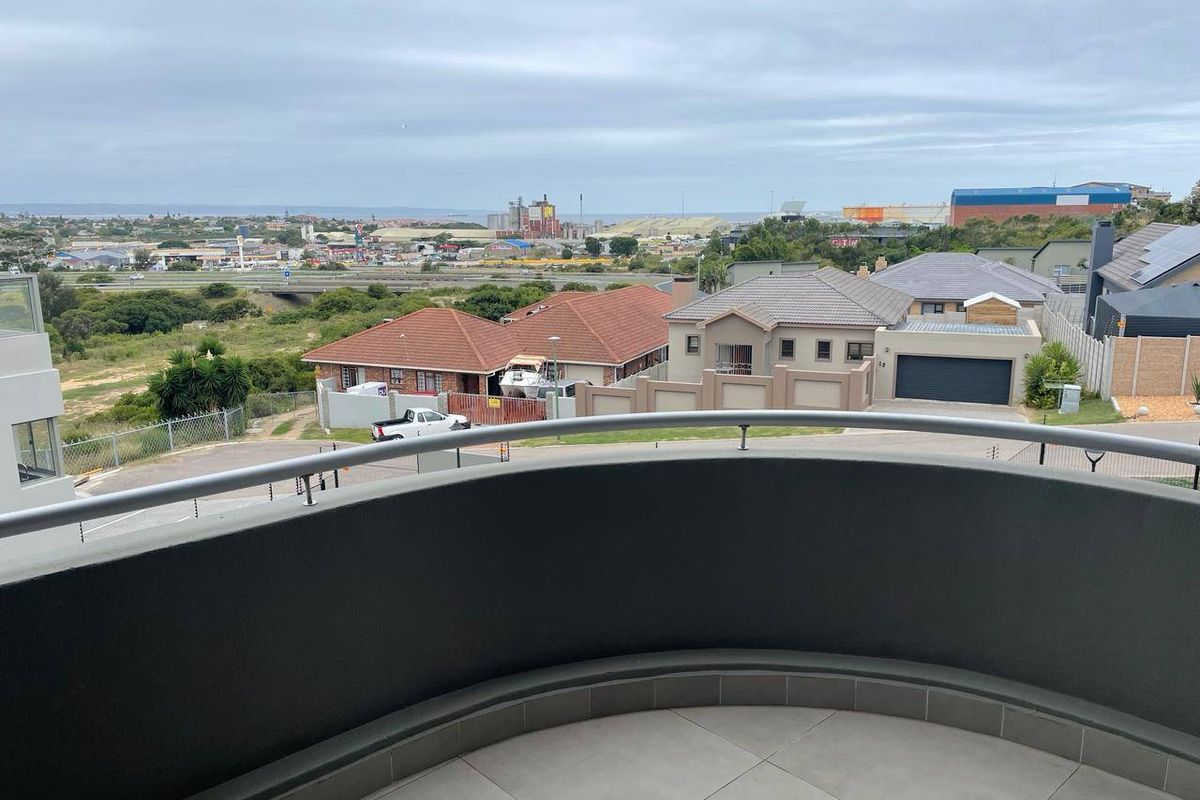 A curved balcony with a modern metal balustrade and tiled flooring, offering an elevated view over the surrounding residential neighborhood.