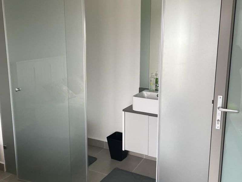 A modern bathroom featuring a wall-mounted vanity with a vessel sink, accessed through a contemporary frosted glass sliding door.
