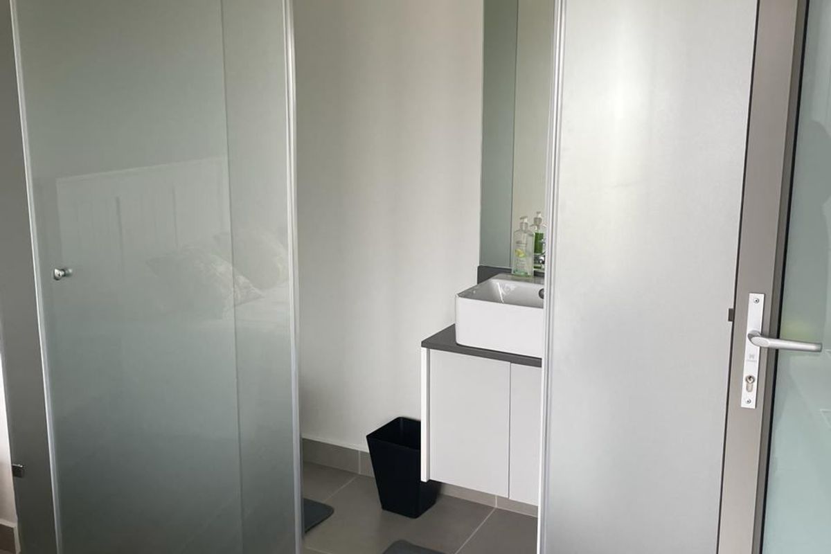 A modern bathroom featuring a wall-mounted vanity with a vessel sink, accessed through a contemporary frosted glass sliding door.