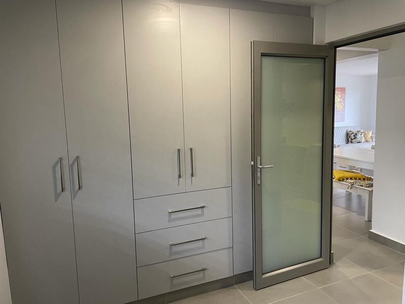 A clean, modern hallway featuring extensive built-in cabinetry with integrated drawers and a contemporary frosted glass door leading to an adjacent living space.