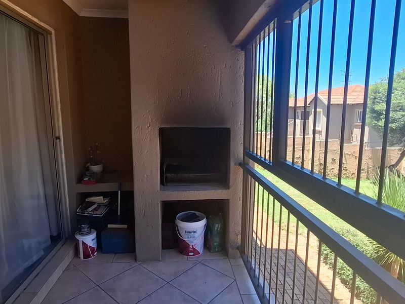 Covered balcony featuring a built-in braai, tiled flooring, and security bars, overlooking the complex garden area.