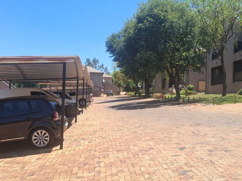 Exterior view of an apartment complex featuring a paved driveway and covered parking bays with metal roofing.