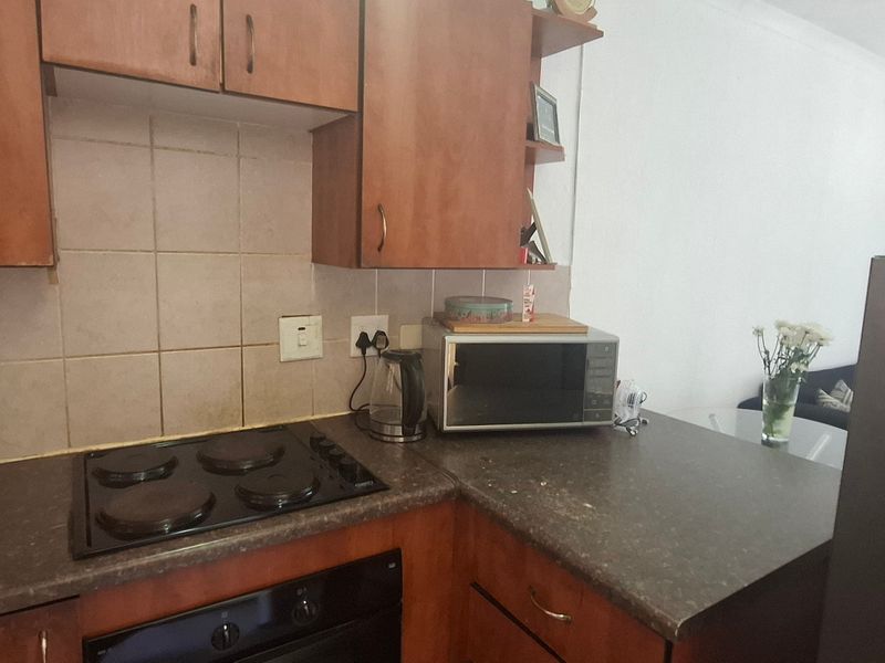 A functional kitchen featuring wooden cabinetry, laminate countertops, a built-in oven, and an electric hob with a tiled backsplash.