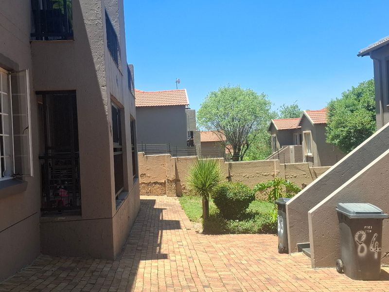 Exterior view of the apartment complex showing a paved walkway, external staircase, and shared garden area with boundary walling.
