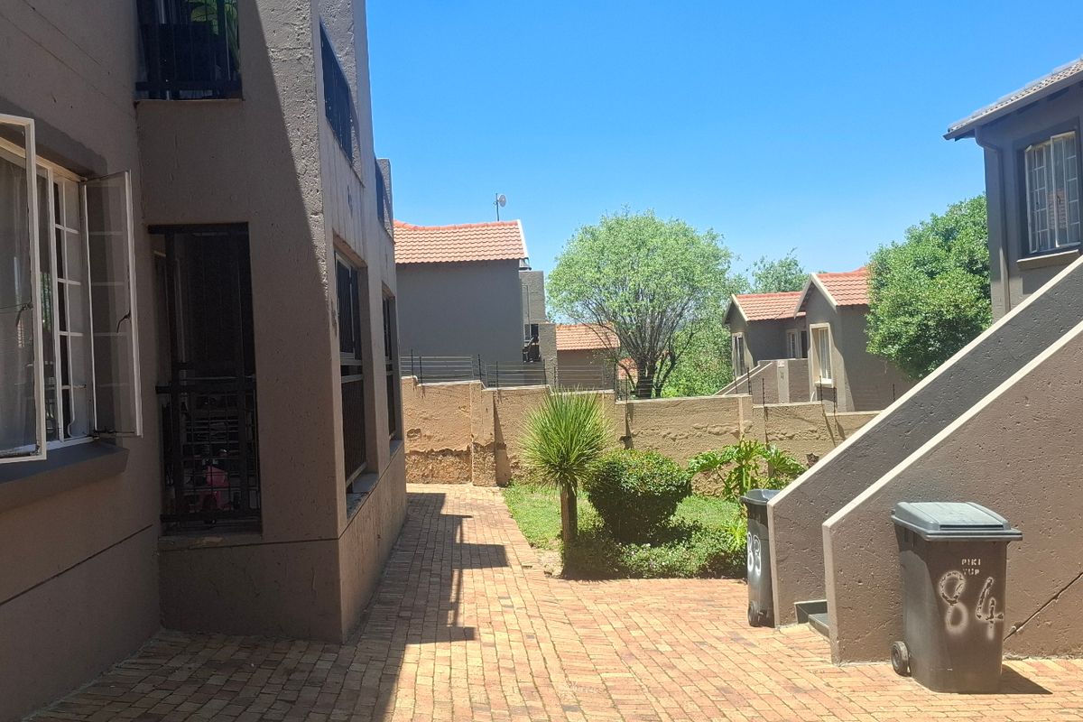 Exterior view of the apartment complex showing a paved walkway, external staircase, and shared garden area with boundary walling.