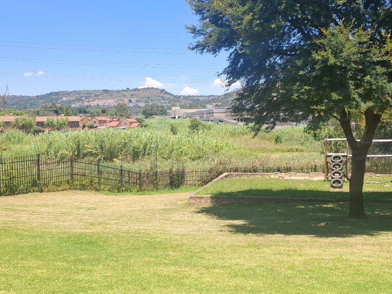 A spacious private garden featuring a well-maintained lawn, mature trees, and metal perimeter fencing with scenic views of the surrounding landscape.