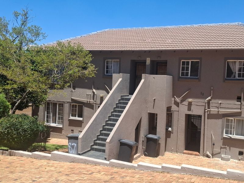 Front elevation of a two-story apartment building featuring a tiled roof, external staircase access, and paved driveway area.