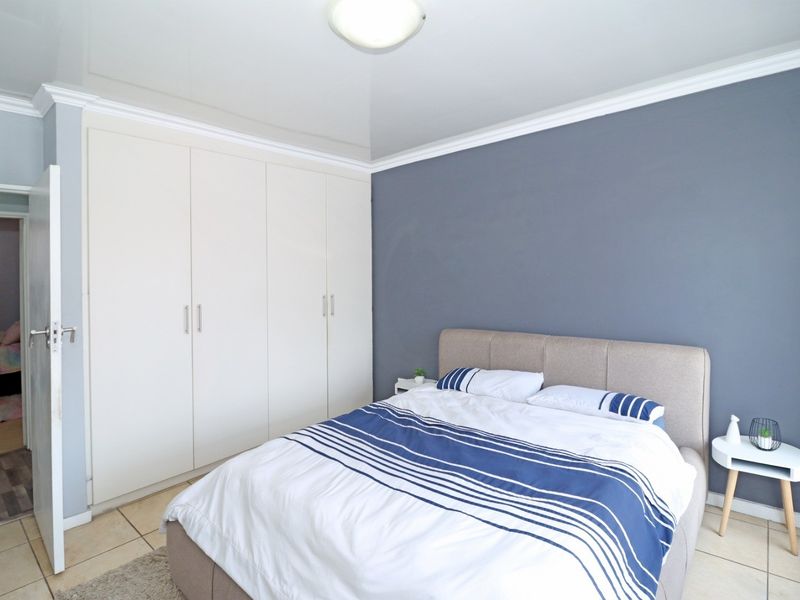 A well-maintained bedroom featuring built-in wardrobes, tiled flooring, and a modern grey accent wall.
