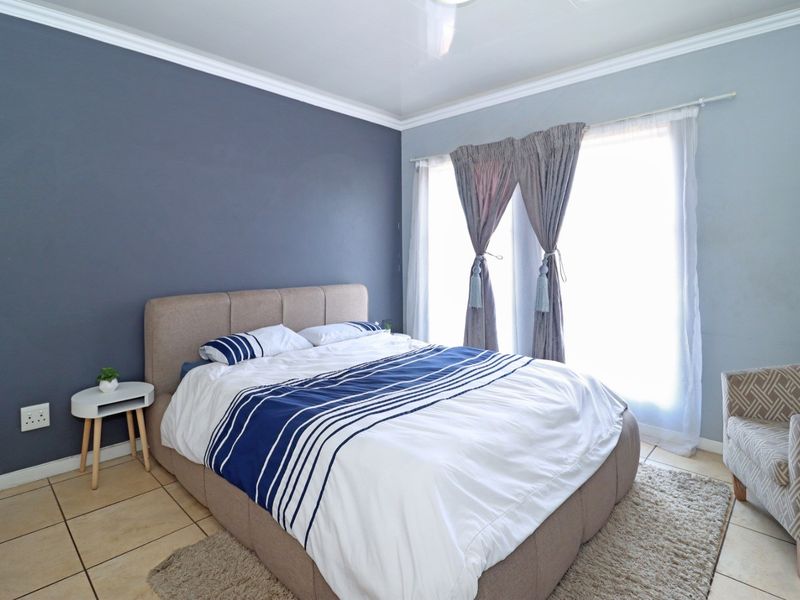 A well-lit bedroom featuring tiled flooring, crown molding, and a large window with curtain tracks.