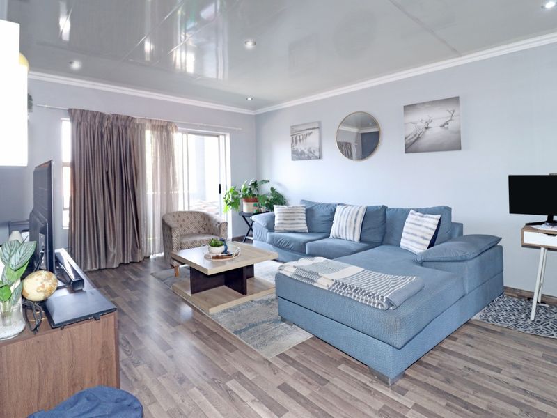 A comfortable living room featuring laminate wood flooring, a high-gloss ceiling finish, and sliding glass doors providing access to an outdoor balcony area.