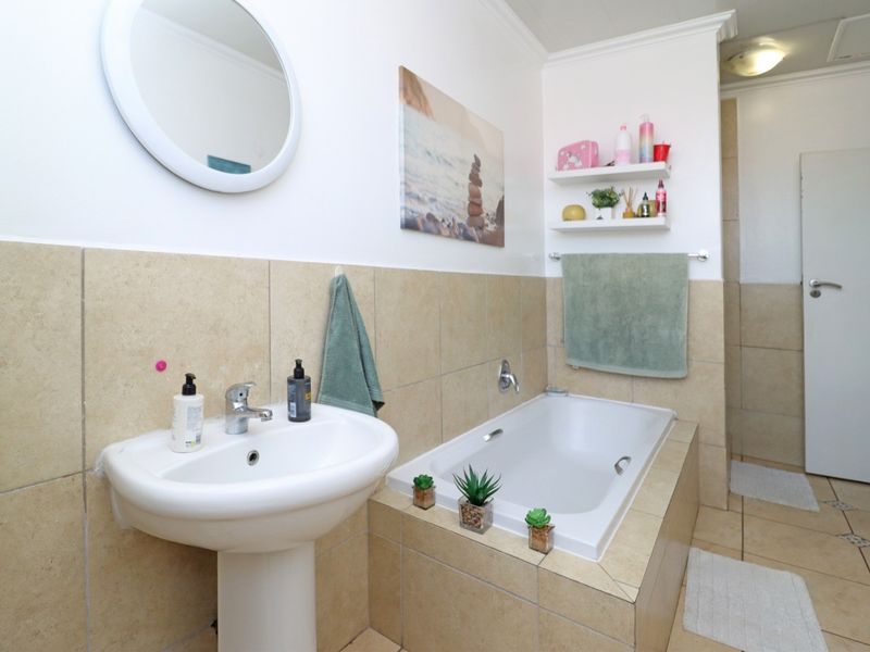 Bathroom featuring a pedestal sink, built-in bathtub with tiled surround, and wall-mounted shelving.