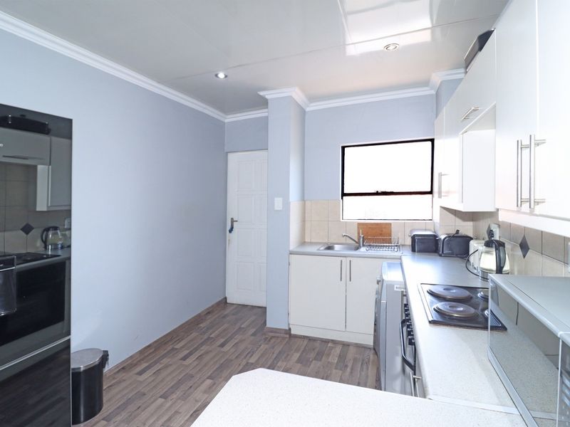 A functional kitchen featuring white cabinetry, a built-in electric hob, a stainless steel sink, and tiled splashbacks with wood-look flooring.
