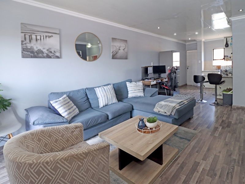 Open-plan living area featuring wood-look laminate flooring, recessed ceiling lighting, and a seamless transition into the kitchen space.