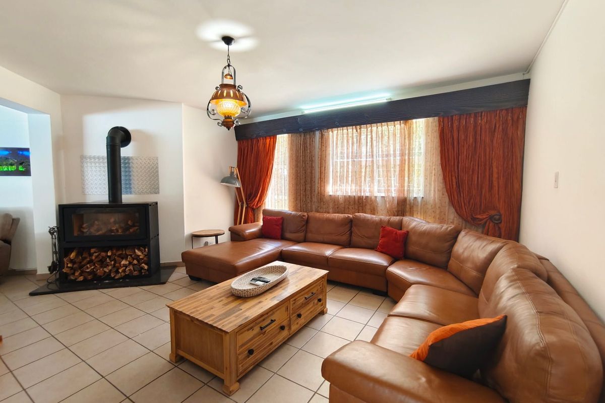 A comfortable living room featuring a modern freestanding fireplace, ceramic tiled flooring, and large windows with decorative drapery.