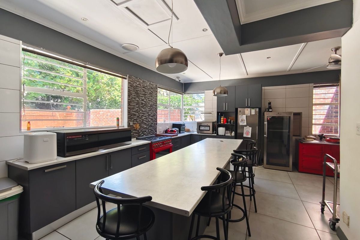 Modern kitchen featuring a large central island with stone countertops, dark cabinetry, mosaic backsplash, and tiled flooring, offering ample workspace and storage.