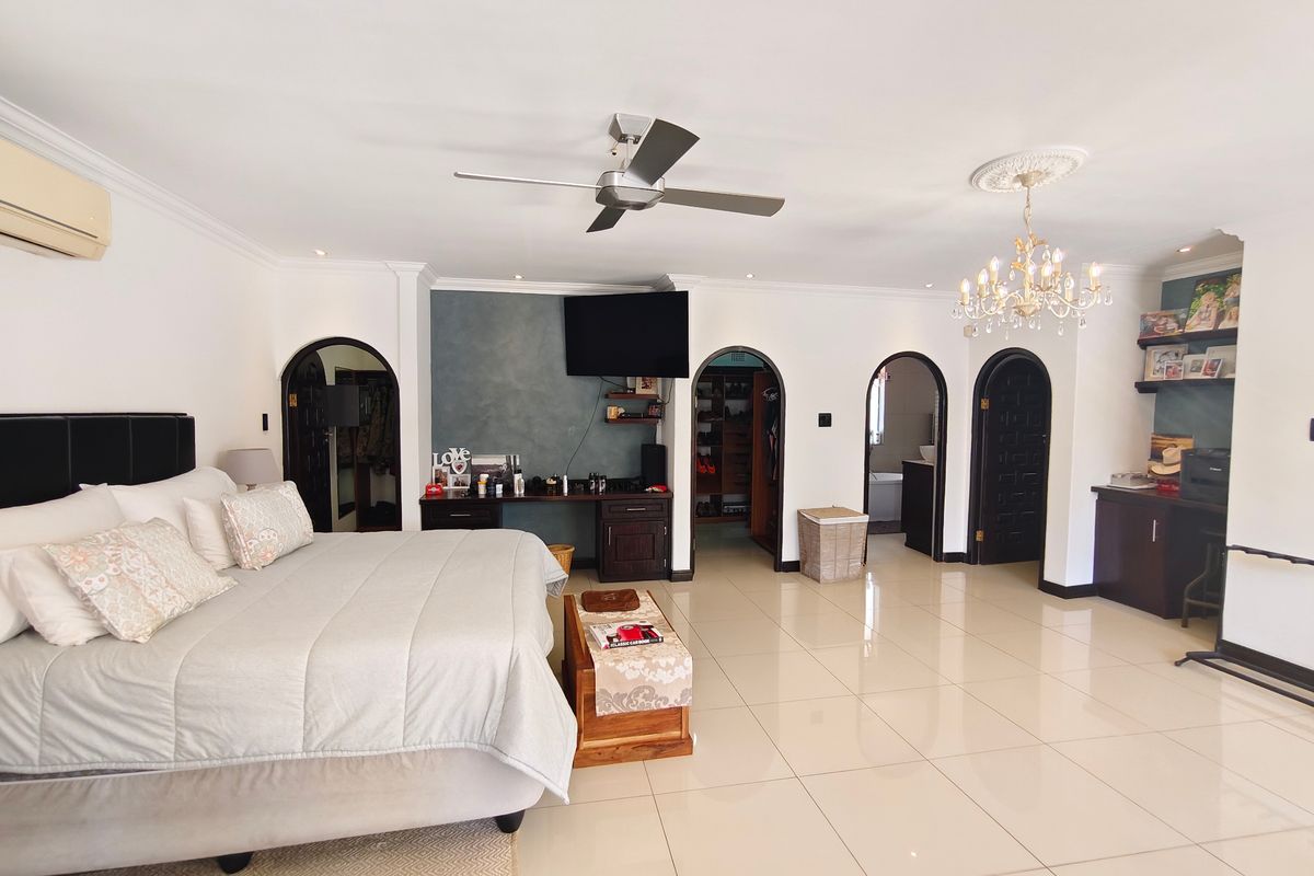Spacious primary bedroom featuring tiled flooring, decorative archway entrances, a ceiling fan, and a crystal chandelier, providing a well-maintained and functional living space.