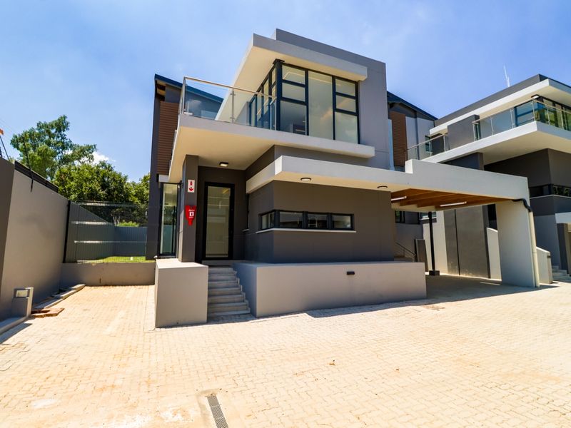 Modern double-story cluster home featuring a paved driveway, covered carport, and an upper-level balcony with glass balustrades.