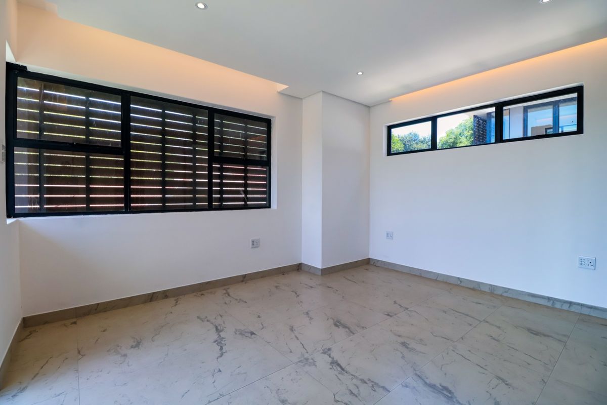 A bright, modern, and empty bedroom featuring large black-framed windows, recessed ceiling lighting, and elegant marble-look porcelain floor tiles.