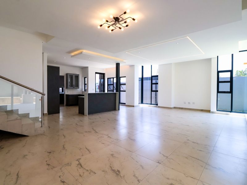 Spacious open-plan living and kitchen area featuring modern marble-look floor tiles, recessed lighting, and a sleek staircase with glass balustrade.