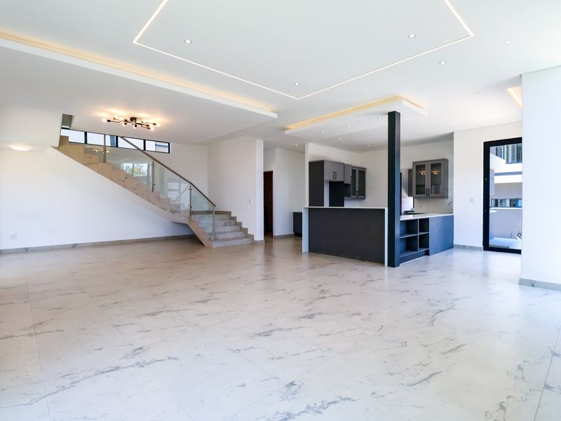 Spacious open-plan living area featuring modern marble-look floor tiles, a sleek kitchen with island, and a contemporary staircase with glass balustrade.
