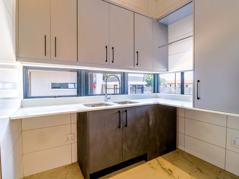 A modern, clean kitchen featuring sleek grey cabinetry, white quartz countertops, a double basin sink, and contemporary tiled finishes.