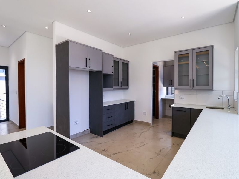 Modern kitchen featuring dark grey cabinetry, white quartz countertops, an induction hob, and an adjoining scullery area with neutral tiled flooring.