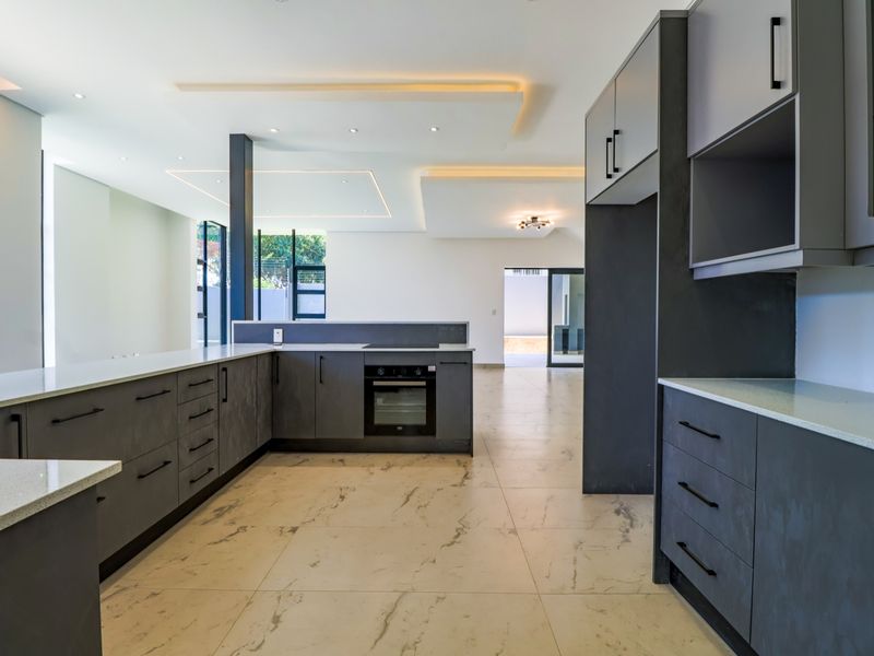 Modern open-plan kitchen featuring sleek dark cabinetry, quartz countertops, built-in oven, hob, and elegant recessed ceiling lighting with large format floor tiles.