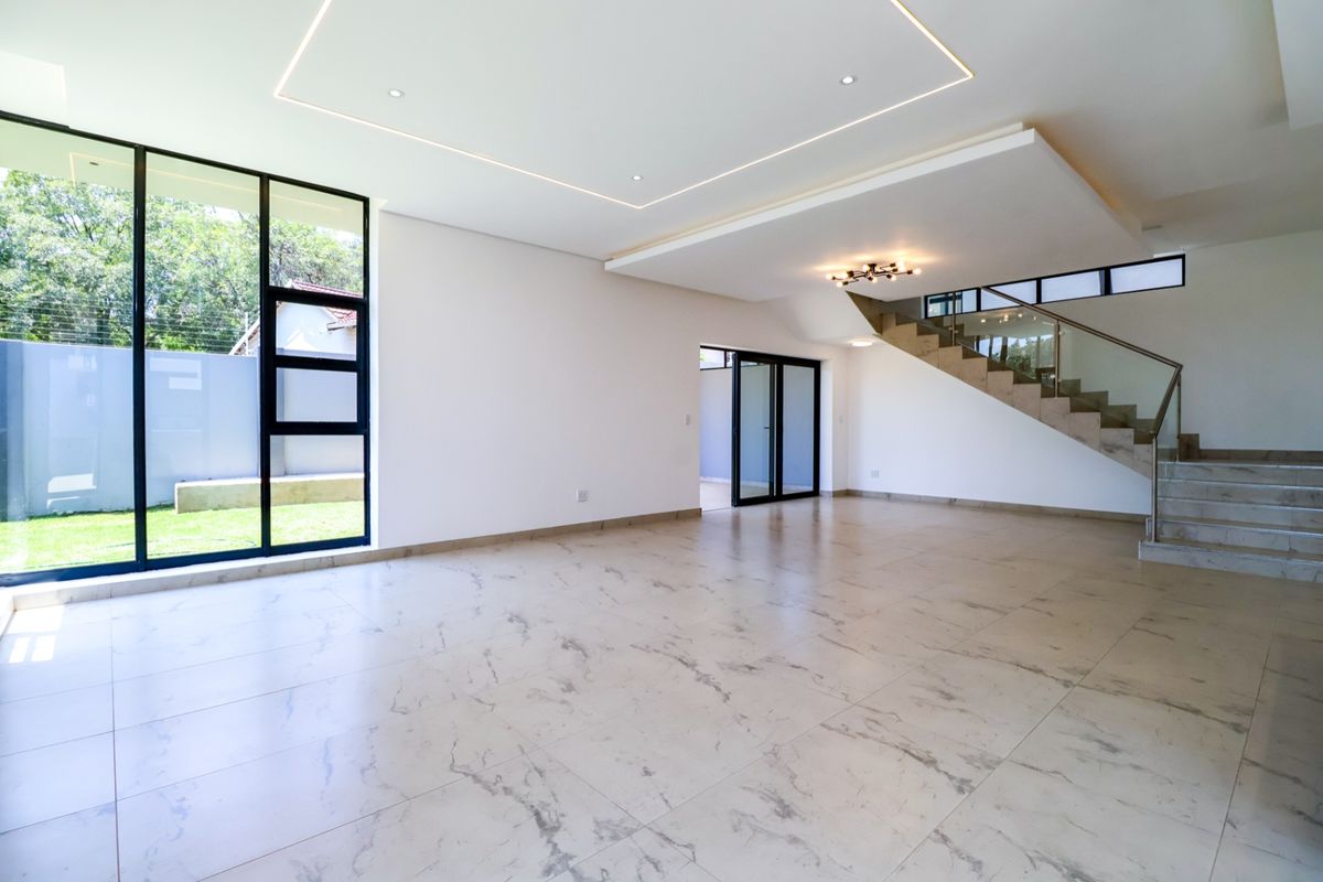 Spacious open-plan living area featuring modern marble-look floor tiles, a striking staircase with glass balustrades, and large windows providing ample natural light.
