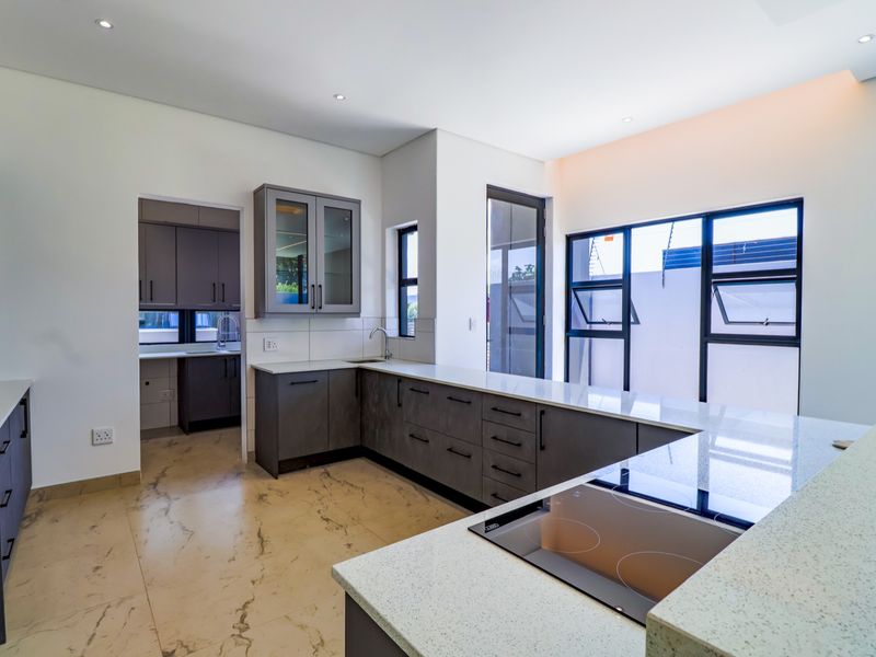 Modern kitchen featuring dark grey cabinetry, stone countertops, an integrated electric hob, and a separate scullery area with ample storage and natural light.