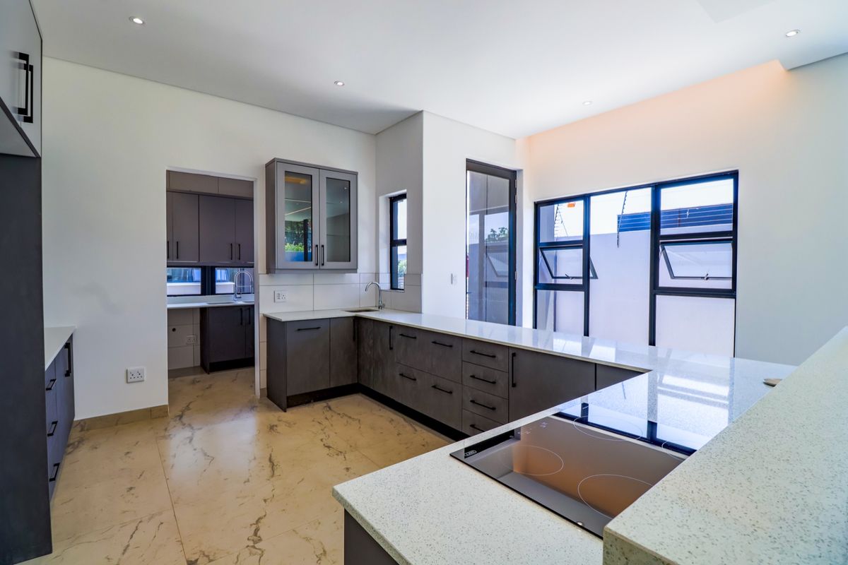 Modern kitchen featuring dark grey cabinetry, stone countertops, an integrated electric hob, and a separate scullery area with ample storage and natural light.