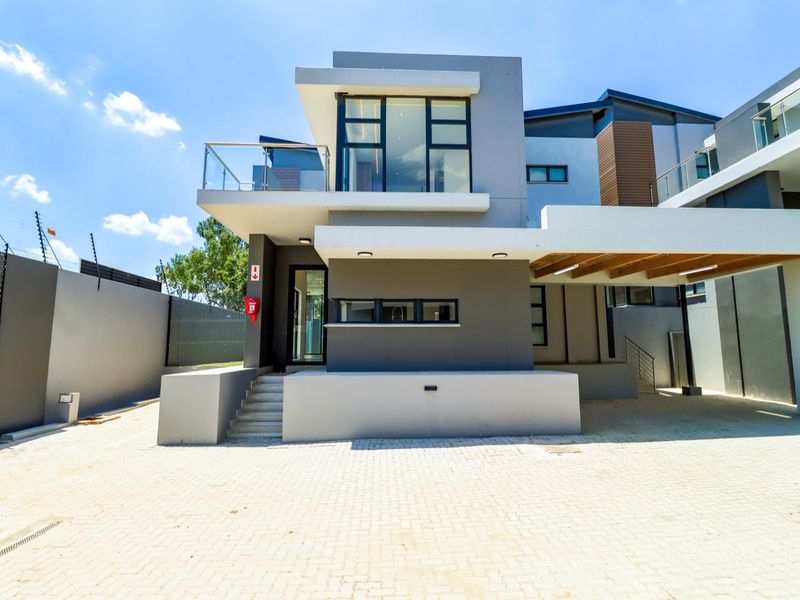 Modern double-story cluster home featuring a paved driveway, covered carport, and a balcony with glass balustrades, showcasing contemporary architectural design.