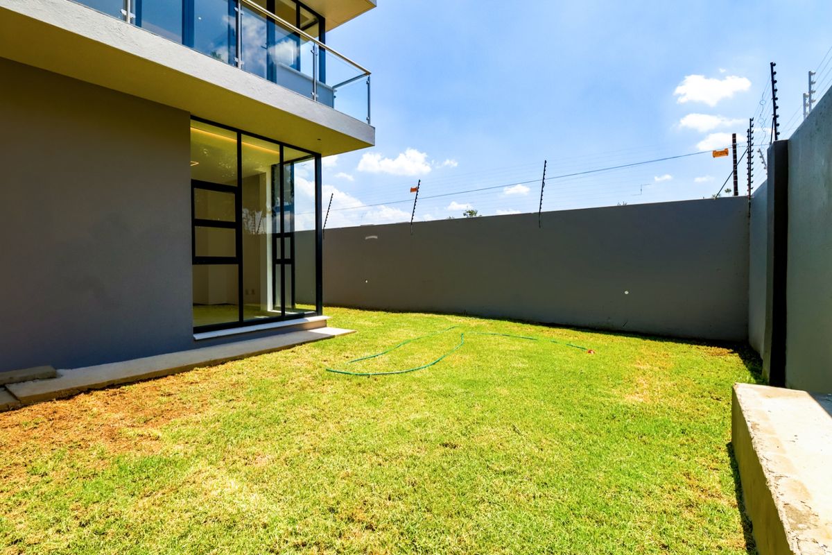 A private rear garden featuring a manicured lawn, high boundary walls with electric fencing, and access to the main dwelling via large glass sliding doors.