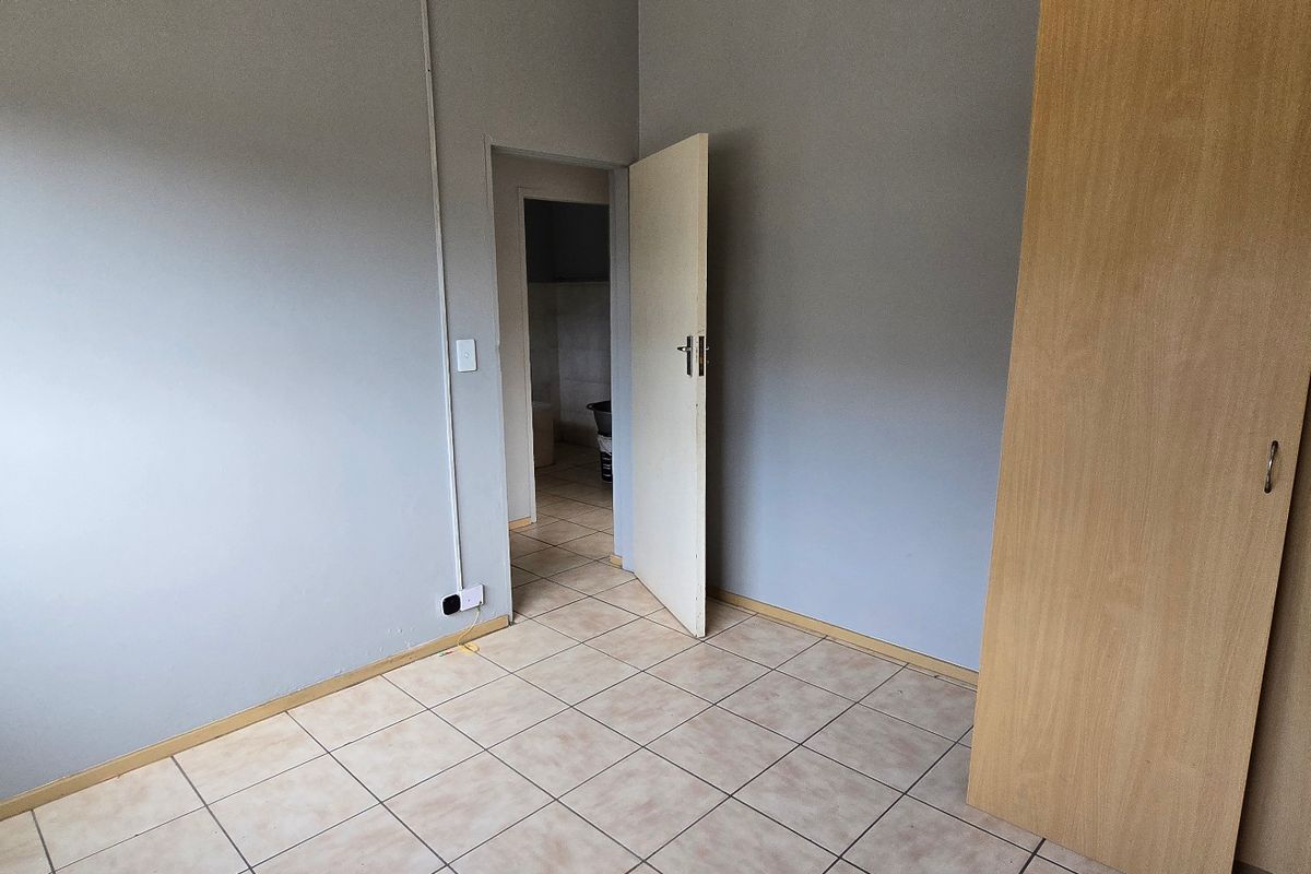 An empty bedroom featuring neutral grey walls, tiled flooring, and a built-in wooden wardrobe.