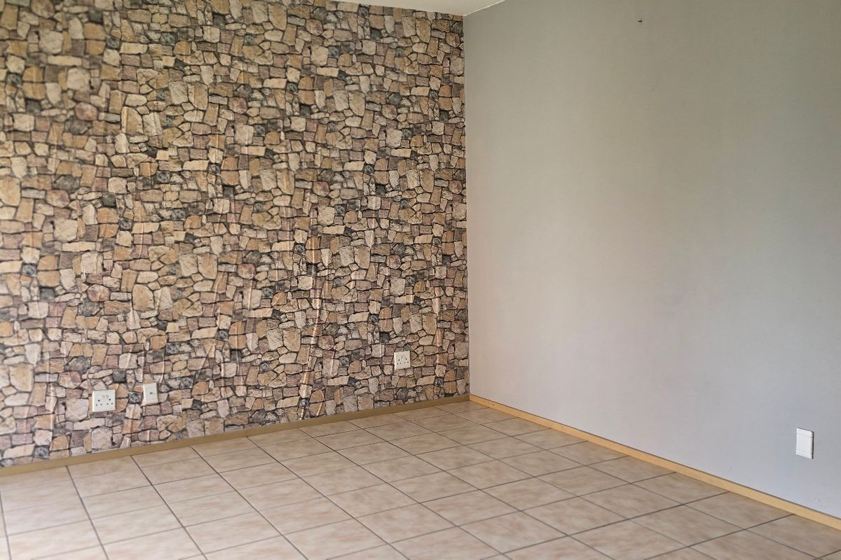 An empty living room featuring tiled flooring and a decorative stone-effect feature wall, providing a neutral base for interior design.