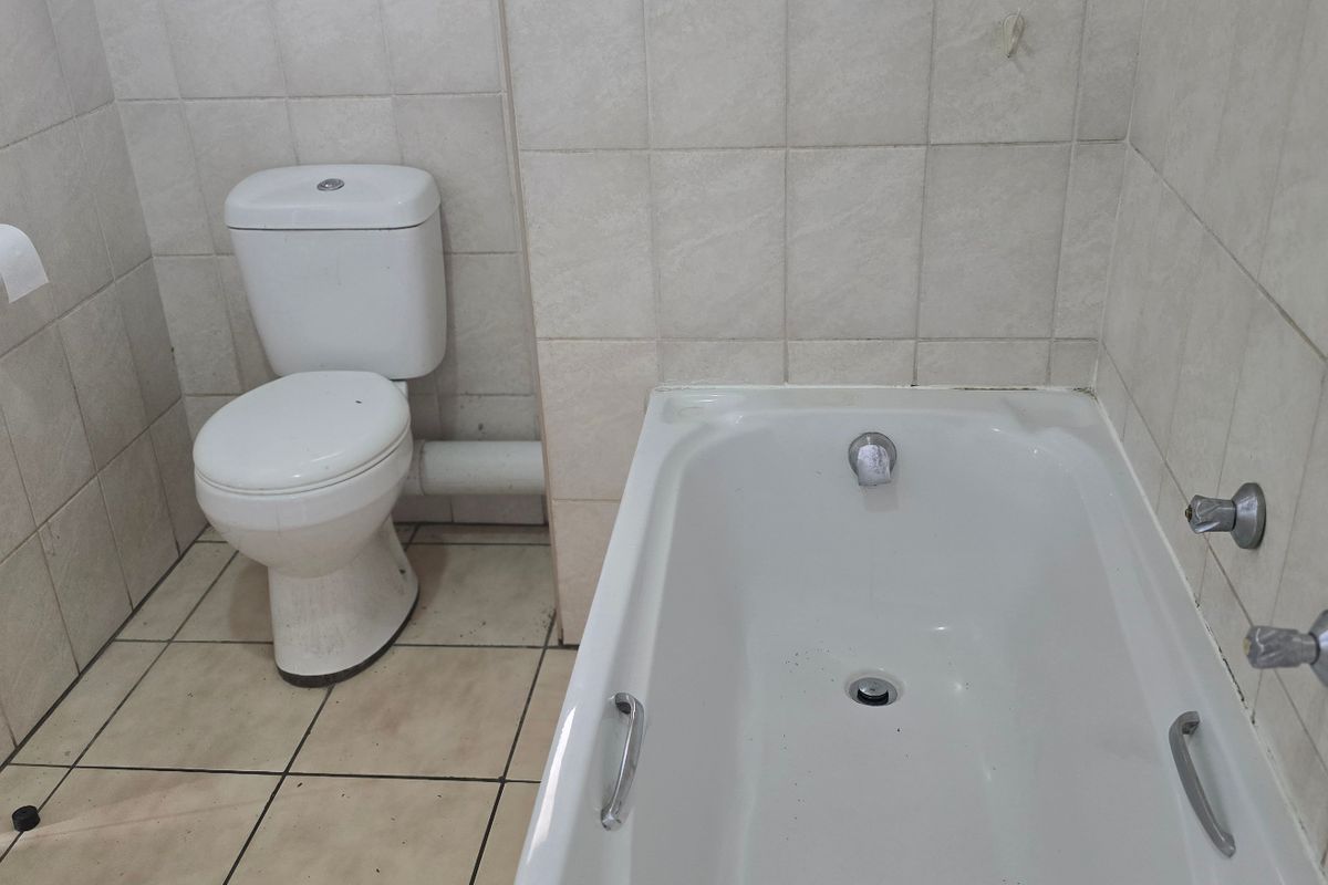 A functional bathroom featuring a standard bathtub and toilet with neutral wall and floor tiling, requiring cosmetic updates to improve its overall condition.