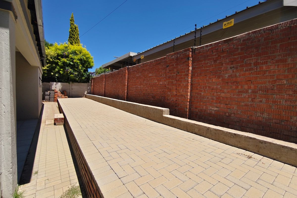 A side exterior walkway featuring paved flooring, a raised concrete retaining wall, and a high brick boundary wall with integrated electric fencing.