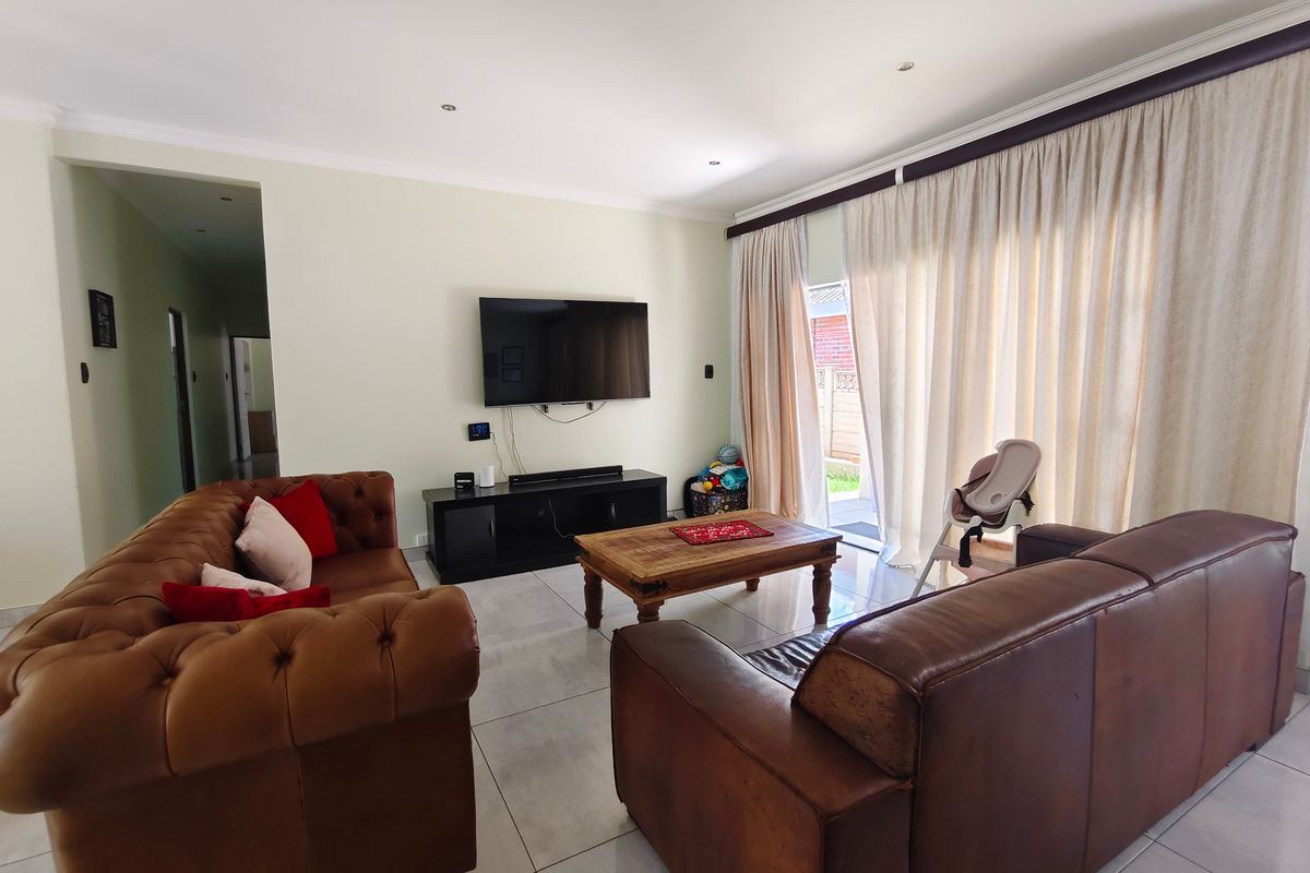 A spacious living room featuring large format floor tiles, recessed lighting, and a sliding glass door providing access to the outdoor area.