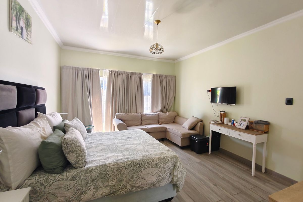 Spacious bedroom featuring laminate flooring, cove cornicing, and a central pendant light fixture, offering a comfortable and well-maintained living space.