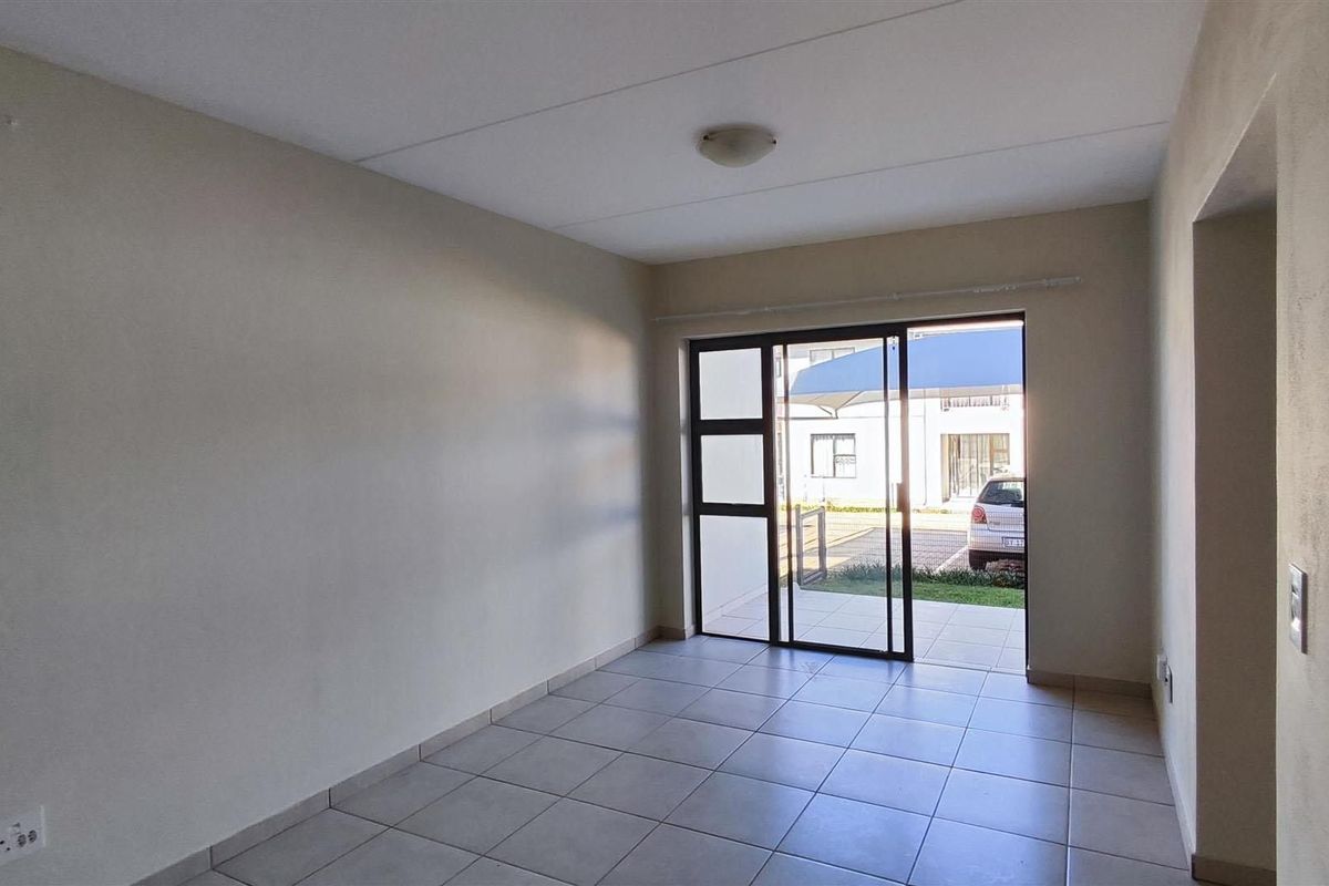 An empty, neutrally painted living room featuring tiled flooring and a sliding glass door providing access to the exterior.